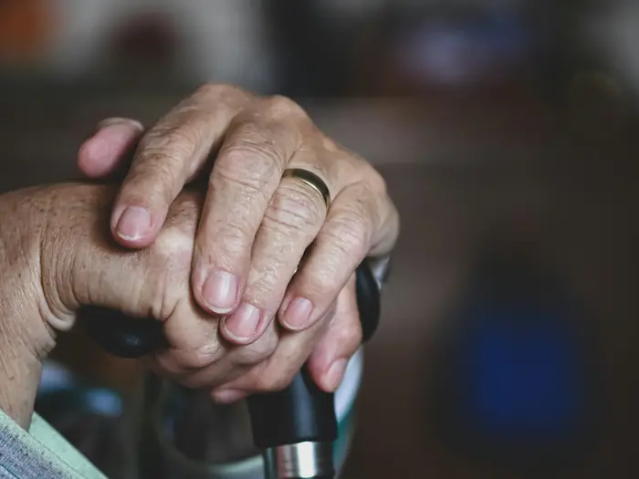 Older hands resting on the handle of a cane