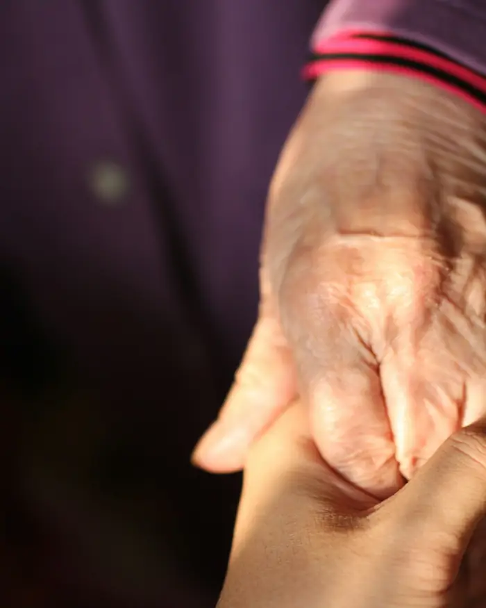 An older person's hand held in a younger person's hands